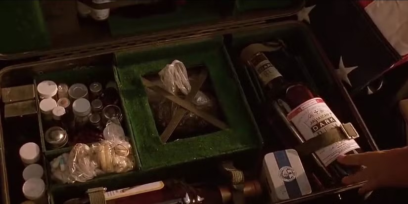 Still from Fear and Loathing in Las Vegas — Duke's open suitcase 'mobile narcotics lab': a green-felt case packed with jars, vials, baggies and a bottle, laid out like a kit