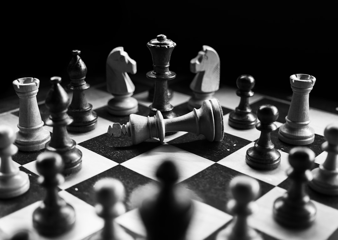 Close-up of a chess board with a toppled white king surrounded by black and white pieces in dramatic high-contrast light